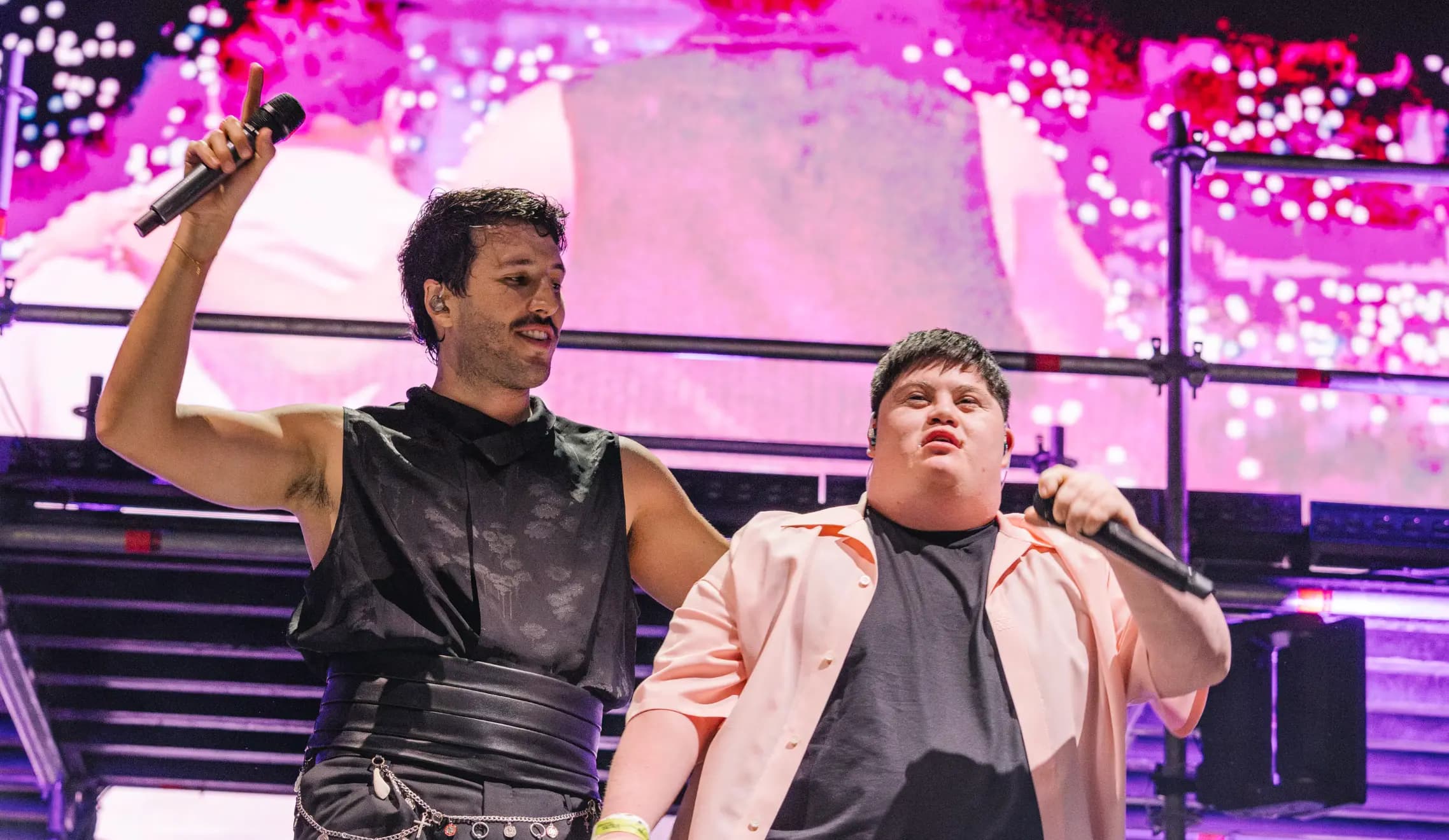 Sebastian Yatra performing live on stage holding a microphone, sharing the stage with a fellow performer in a vibrant concert setting.